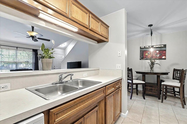 kitchen with brown cabinets, a sink, light countertops, light tile patterned flooring, and a ceiling fan