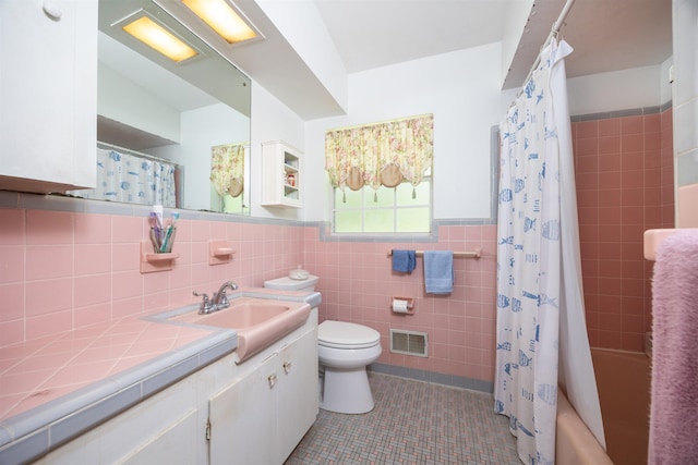 full bathroom with shower / tub combo with curtain, tile walls, tile patterned flooring, vanity, and toilet