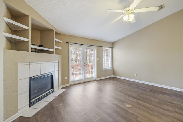 unfurnished living room with baseboards, a ceiling fan, a tiled fireplace, wood finished floors, and a textured ceiling