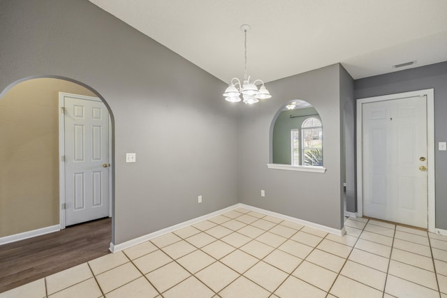 empty room with a notable chandelier, vaulted ceiling, visible vents, and light tile patterned floors