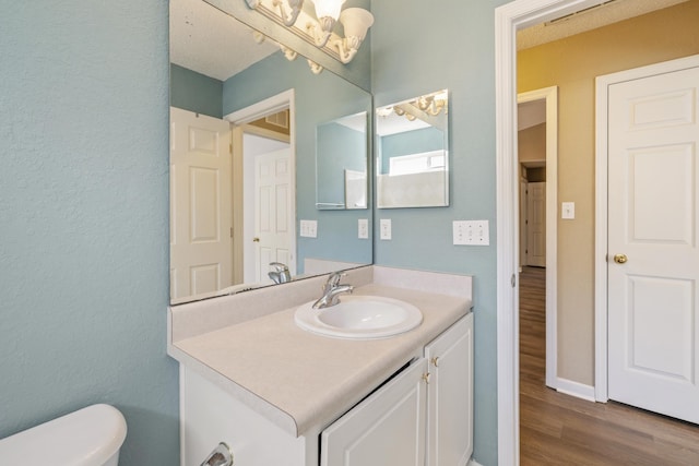 half bath featuring vanity, wood finished floors, toilet, and baseboards