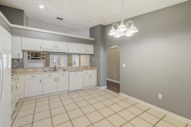 kitchen with white appliances, tasteful backsplash, arched walkways, light countertops, and a sink