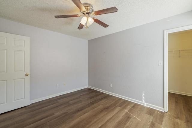 unfurnished bedroom featuring baseboards, wood finished floors, a spacious closet, a textured ceiling, and a closet