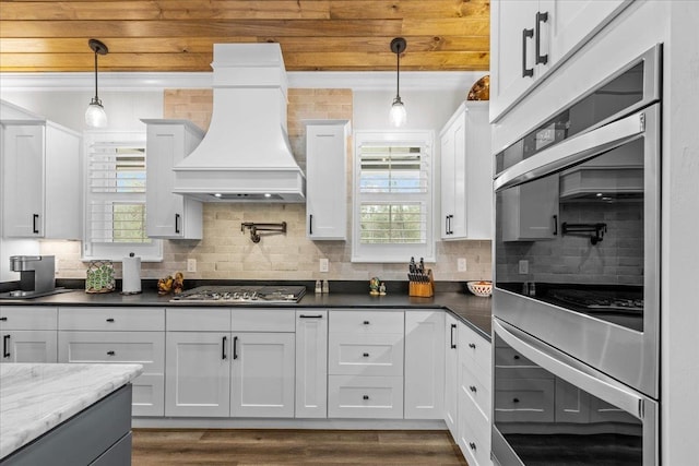 kitchen featuring backsplash, appliances with stainless steel finishes, dark stone counters, white cabinets, and custom exhaust hood