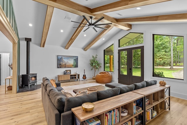 living room featuring french doors, vaulted ceiling with beams, a wood stove, light wood-type flooring, and ceiling fan