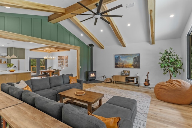 living room with light wood-type flooring, a wood stove, ceiling fan, and lofted ceiling with beams