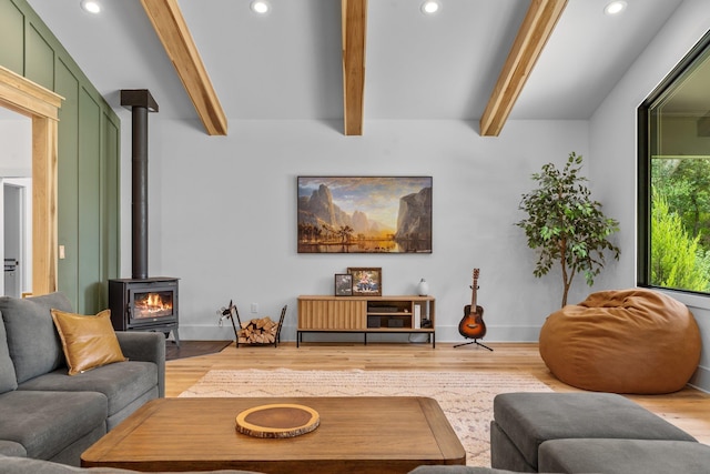 living room featuring a wood stove, beamed ceiling, and wood-type flooring