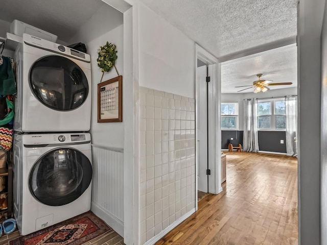 washroom featuring ceiling fan, stacked washer and clothes dryer, a textured ceiling, and light hardwood / wood-style flooring