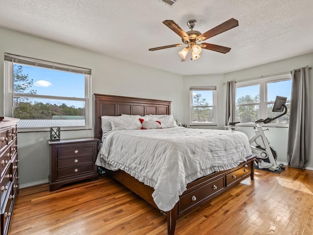 bedroom with ceiling fan, light hardwood / wood-style floors, and a textured ceiling