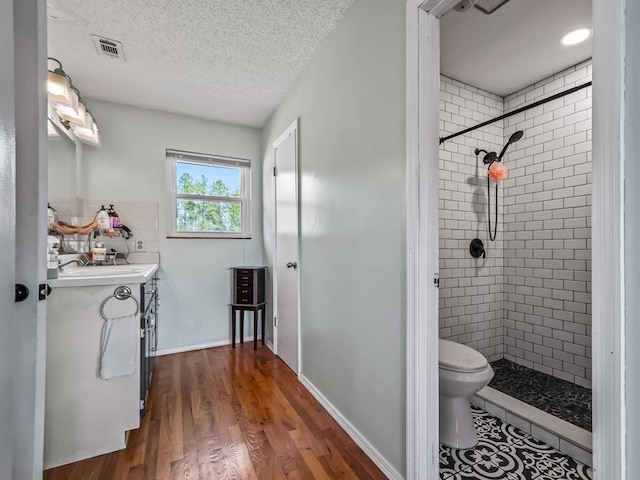 bathroom with hardwood / wood-style flooring, vanity, a textured ceiling, and a tile shower