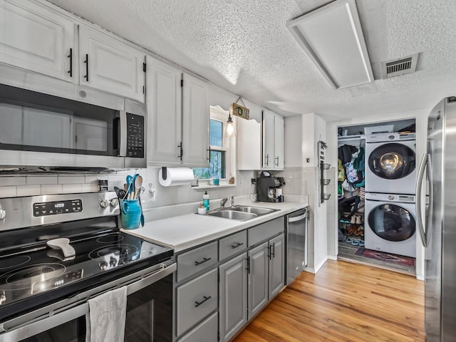 kitchen featuring sink, light hardwood / wood-style flooring, stacked washing maching and dryer, white cabinetry, and stainless steel appliances