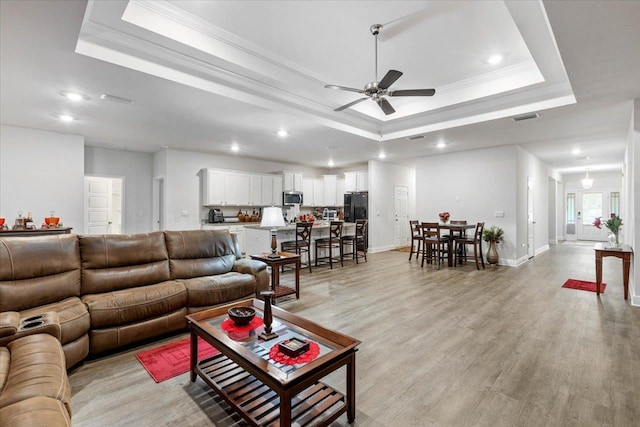 living room with crown molding, a tray ceiling, ceiling fan, and light wood-type flooring