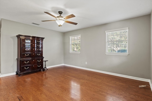 spare room with wood finished floors, a ceiling fan, visible vents, and baseboards