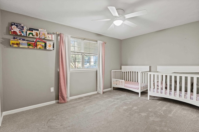 bedroom with baseboards, a nursery area, a ceiling fan, and carpet flooring