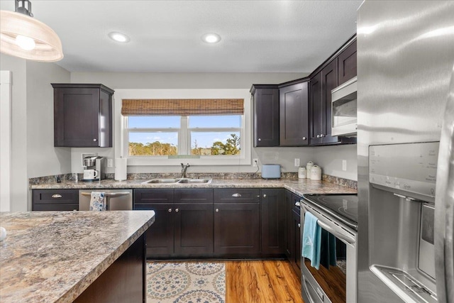 kitchen with dark brown cabinetry, appliances with stainless steel finishes, sink, and light hardwood / wood-style flooring