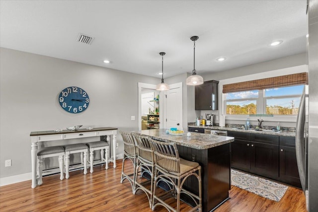 kitchen featuring a kitchen island, a breakfast bar, sink, hanging light fixtures, and hardwood / wood-style flooring