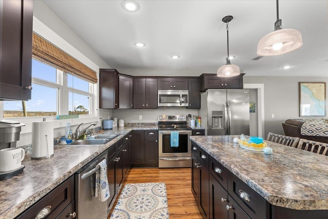 kitchen featuring sink, light wood-type flooring, a kitchen island, pendant lighting, and stainless steel appliances