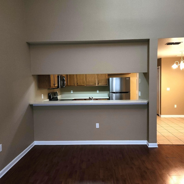 kitchen featuring appliances with stainless steel finishes, brown cabinets, wood finished floors, baseboards, and light countertops