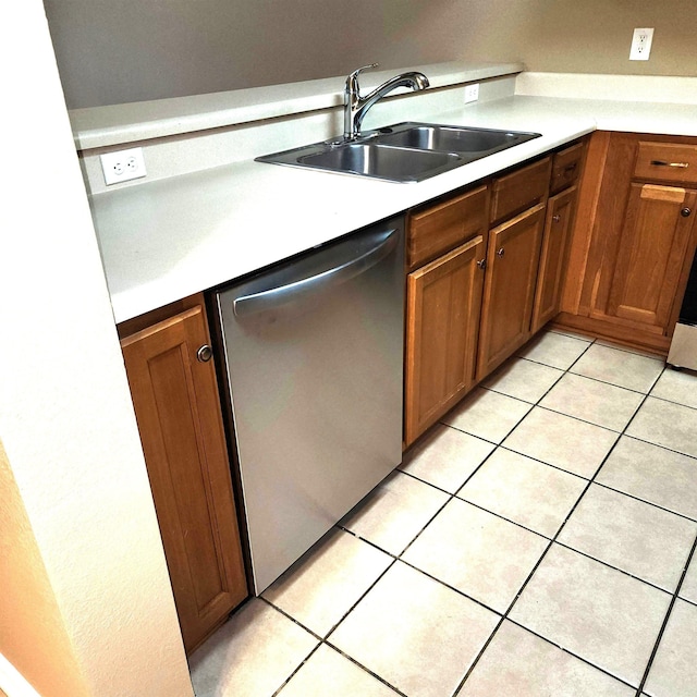 kitchen featuring stainless steel dishwasher, a sink, light countertops, light tile patterned flooring, and brown cabinetry