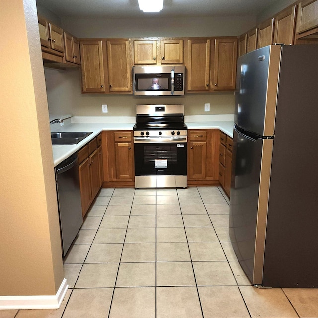 kitchen with stainless steel appliances, a sink, brown cabinetry, light countertops, and light tile patterned floors