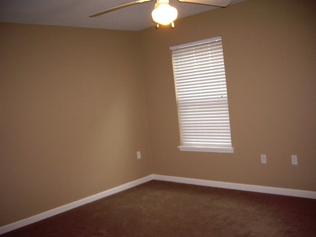 spare room with a ceiling fan, dark colored carpet, and baseboards