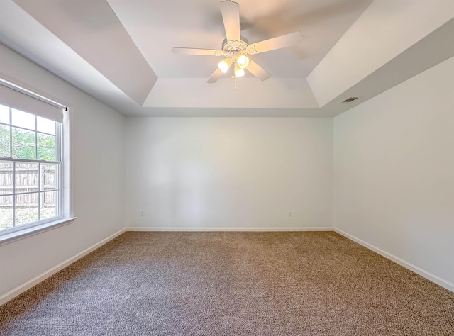 carpeted spare room with a ceiling fan, a tray ceiling, visible vents, and baseboards