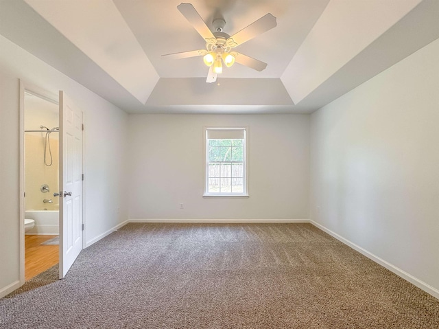 carpeted empty room with baseboards, a raised ceiling, and ceiling fan