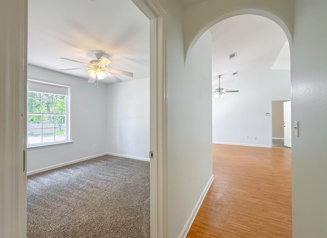 hallway with arched walkways, baseboards, visible vents, and lofted ceiling