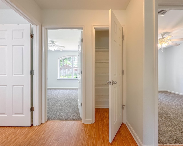 hallway with light wood-type flooring, baseboards, and light carpet