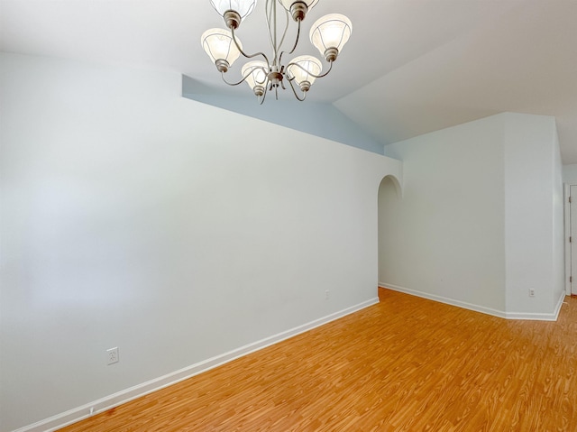 spare room with a chandelier, arched walkways, baseboards, lofted ceiling, and light wood-style floors