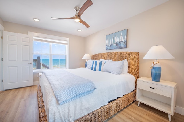 bedroom with light hardwood / wood-style flooring, ceiling fan, and a water view