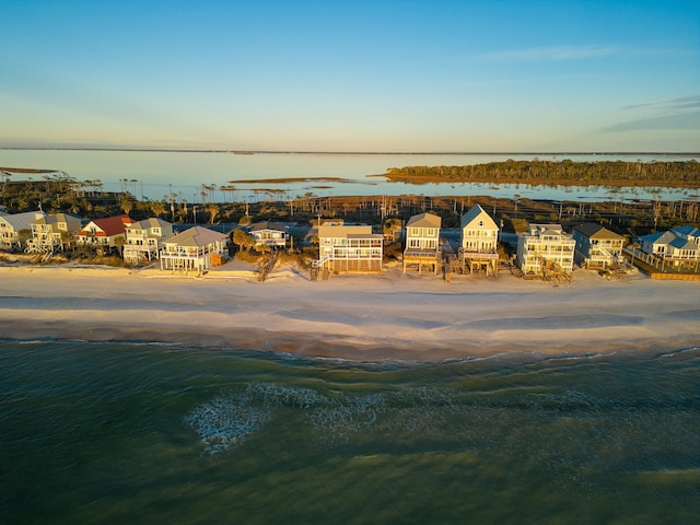 aerial view at dusk featuring a water view and a beach view