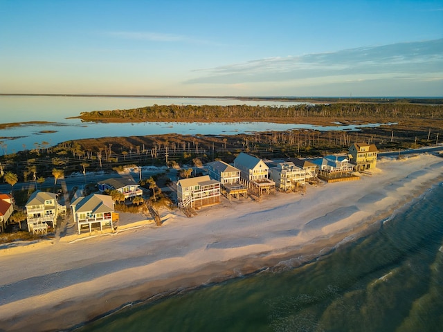 aerial view at dusk featuring a water view and a beach view