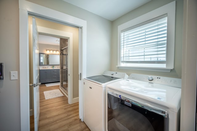 laundry room with sink, washing machine and clothes dryer, and light wood-type flooring