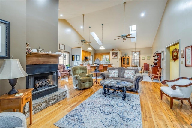 living area with a skylight, ceiling fan, light wood finished floors, and a fireplace with raised hearth