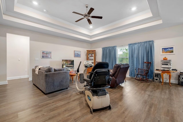 living room featuring ceiling fan, a raised ceiling, and wood-type flooring