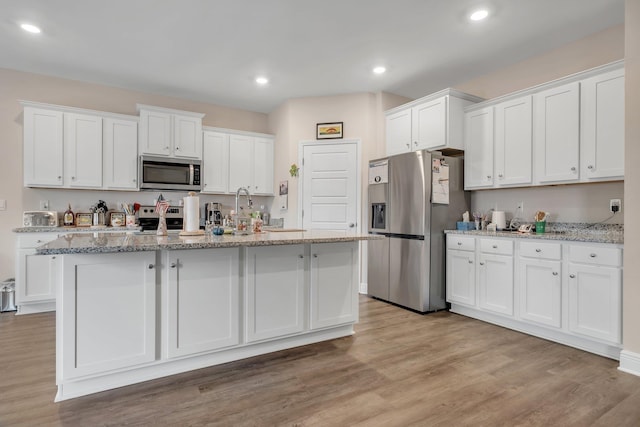 kitchen with white cabinets, appliances with stainless steel finishes, light wood-type flooring, and light stone countertops