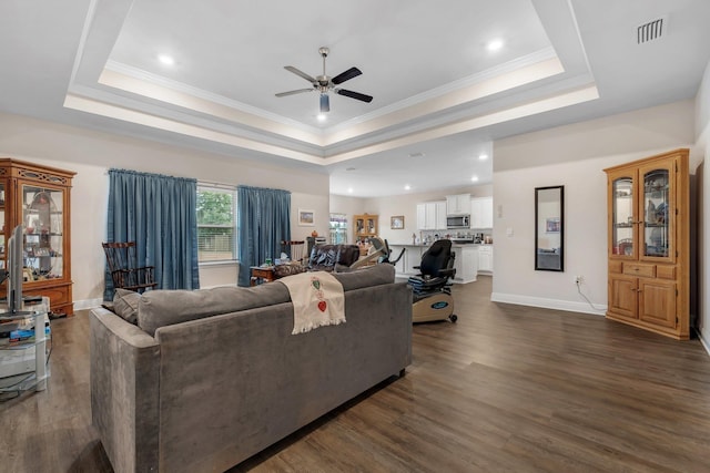 living room with a raised ceiling, ceiling fan, and dark wood-type flooring