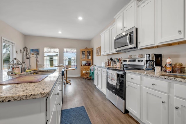 kitchen with white cabinetry, stainless steel appliances, light stone counters, and light wood-type flooring