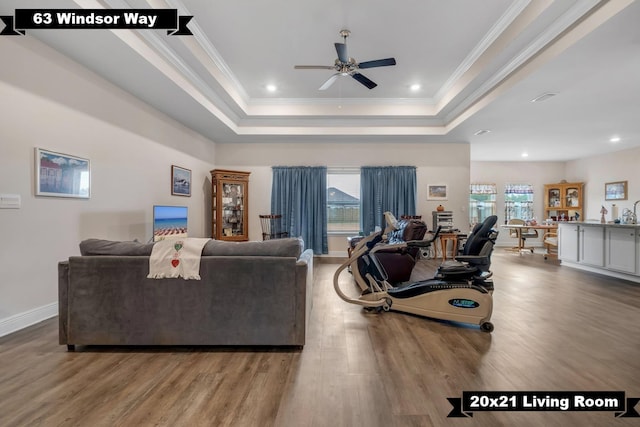 living room with a raised ceiling, crown molding, hardwood / wood-style floors, and ceiling fan