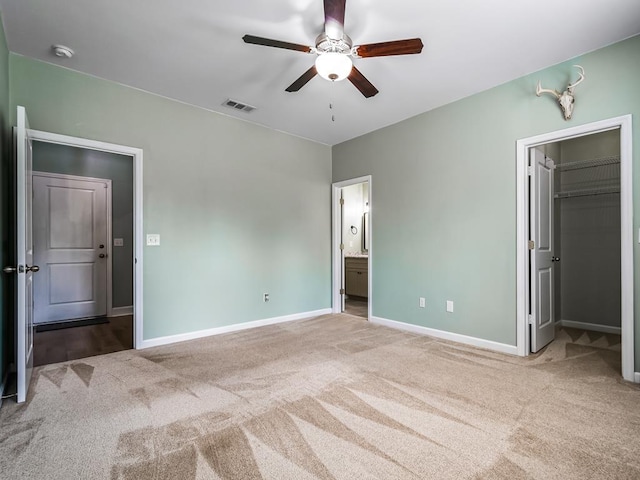 unfurnished bedroom featuring connected bathroom, a spacious closet, light colored carpet, and ceiling fan