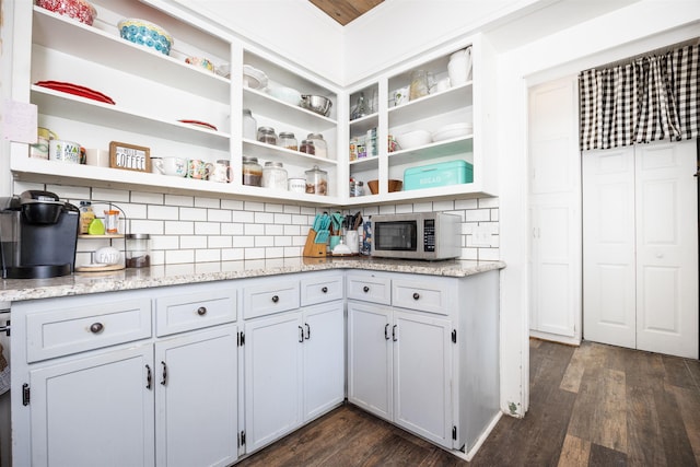 kitchen with tasteful backsplash, light stone countertops, and dark wood-type flooring