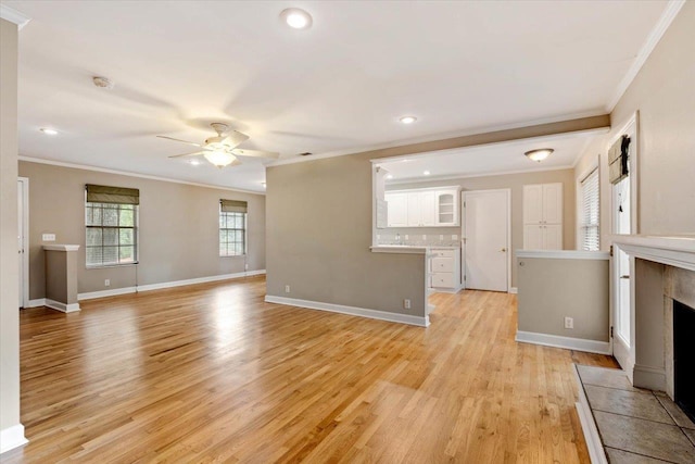 unfurnished living room featuring light hardwood / wood-style flooring, ornamental molding, a tile fireplace, and ceiling fan