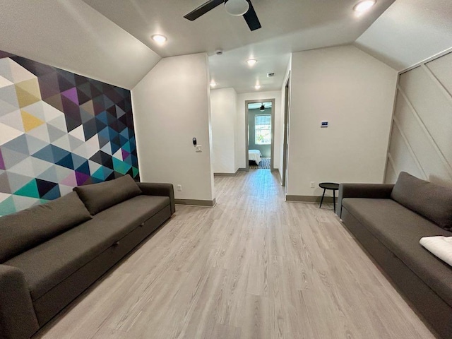 living room with vaulted ceiling, light wood-type flooring, a ceiling fan, and an accent wall