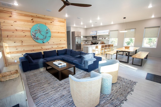 living area featuring visible vents, recessed lighting, light wood-style flooring, and wood walls