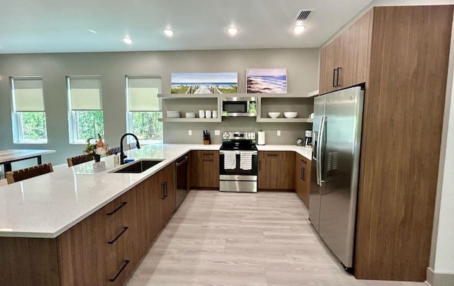 kitchen with a sink, light stone countertops, stainless steel appliances, modern cabinets, and a peninsula