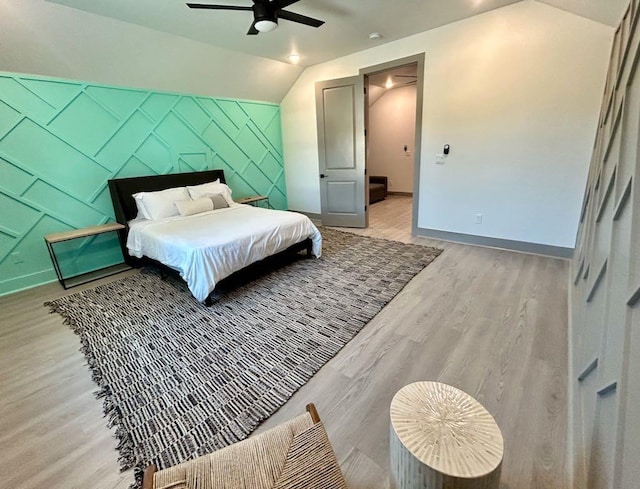 bedroom featuring ceiling fan, baseboards, vaulted ceiling, light wood-style floors, and an accent wall