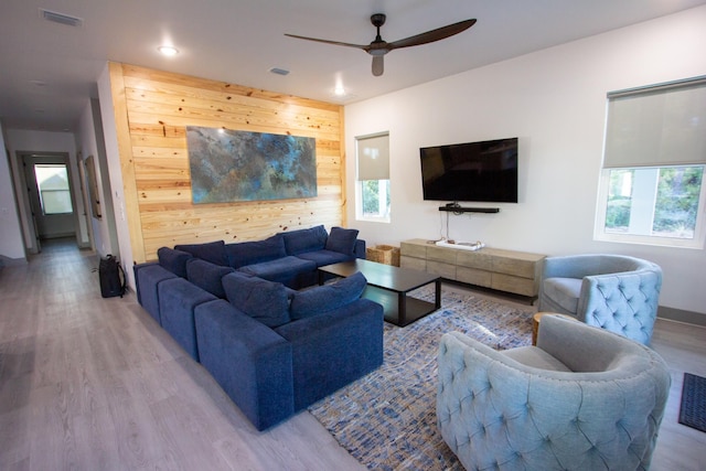 living room featuring ceiling fan, visible vents, light wood-style floors, and wood walls