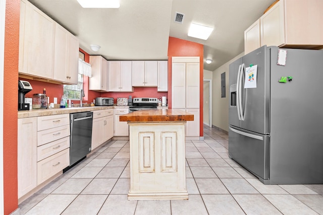 kitchen with appliances with stainless steel finishes, light tile patterned floors, a kitchen island, and vaulted ceiling