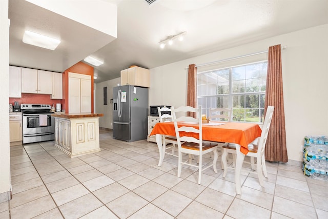 kitchen with vaulted ceiling, cream cabinetry, light tile patterned floors, and appliances with stainless steel finishes